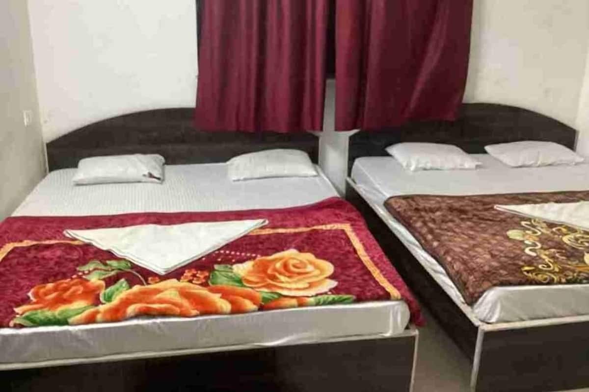 Zwei Einzelbetten mit weißen Laken, ein roter Vorhang und eine blumige Tagesdecke auf einem Bett.