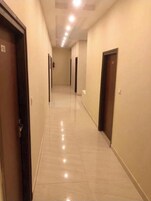Un pasillo largo y estrecho con puertas a ambos lados, suelo de baldosas e iluminación empotrada en el techo.