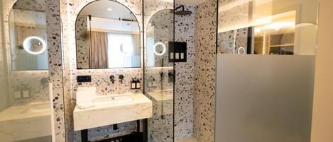 Un baño moderno con cabina de ducha de vidrio, un lavabo de mármol blanco y un espejo grande.