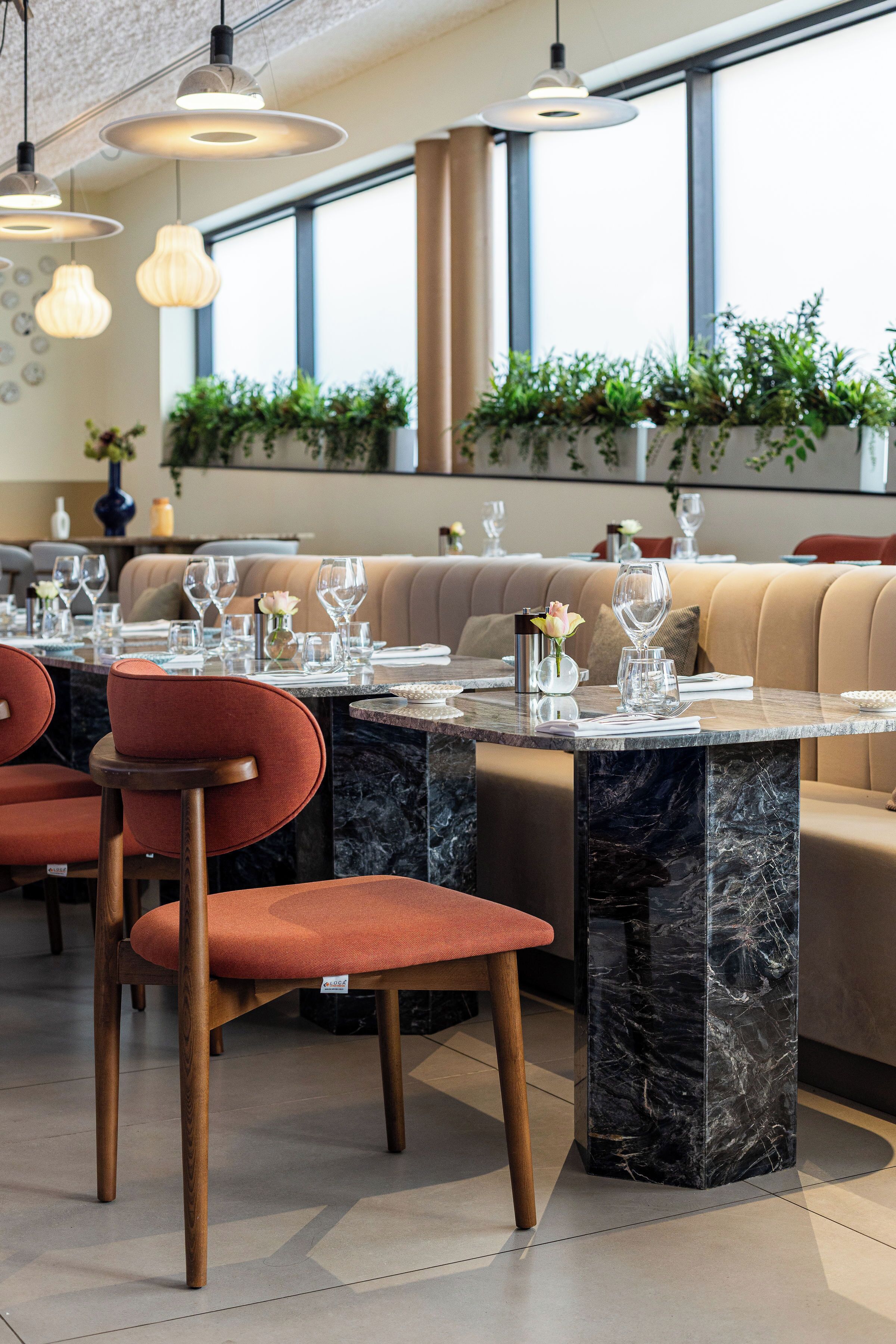 Un restaurante con mesas de mármol, asientos acolchados, iluminación colgante y plantas en macetas.