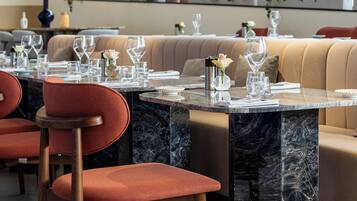Un restaurant avec des tables en marbre, des sièges rembourrés, des luminaires suspendus et des plantes en pot.