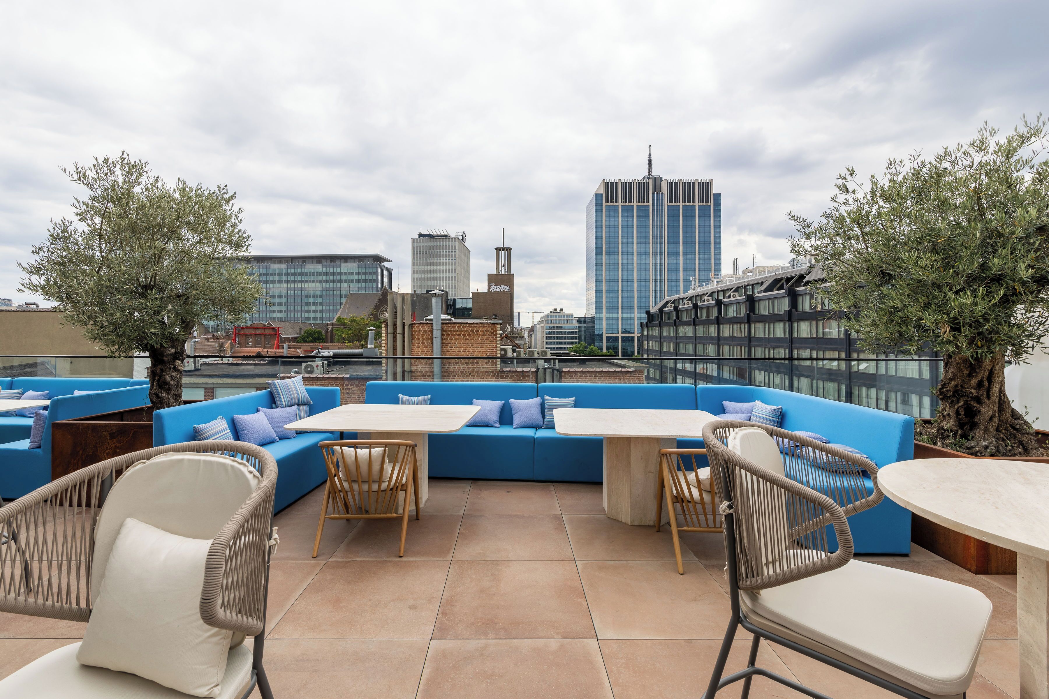 A rooftop terrace with blue seating, wicker chairs, and a view of city buildings.