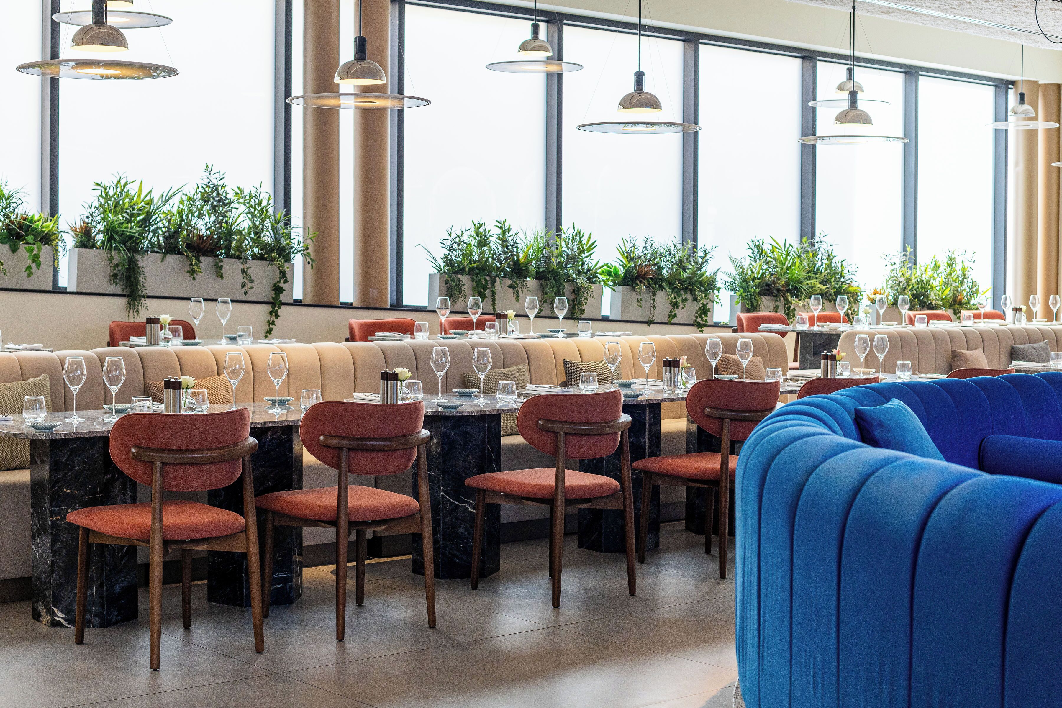 A restaurant with a long communal dining table, individual dining booths, and a blue sofa.
