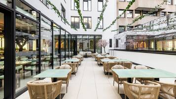 A modern indoor dining area with glass walls, wicker furniture, and a central seating arrangement.
