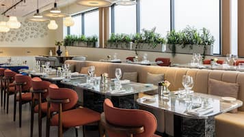 Un restaurante con una larga mesa de comedor, sillas rojas y una zona de bar.
