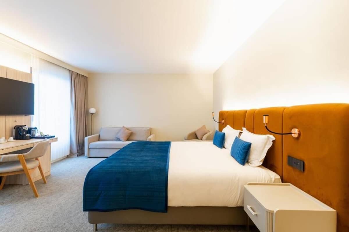 A hotel room with a bed, a desk, a chair, a television, and a bedside table.