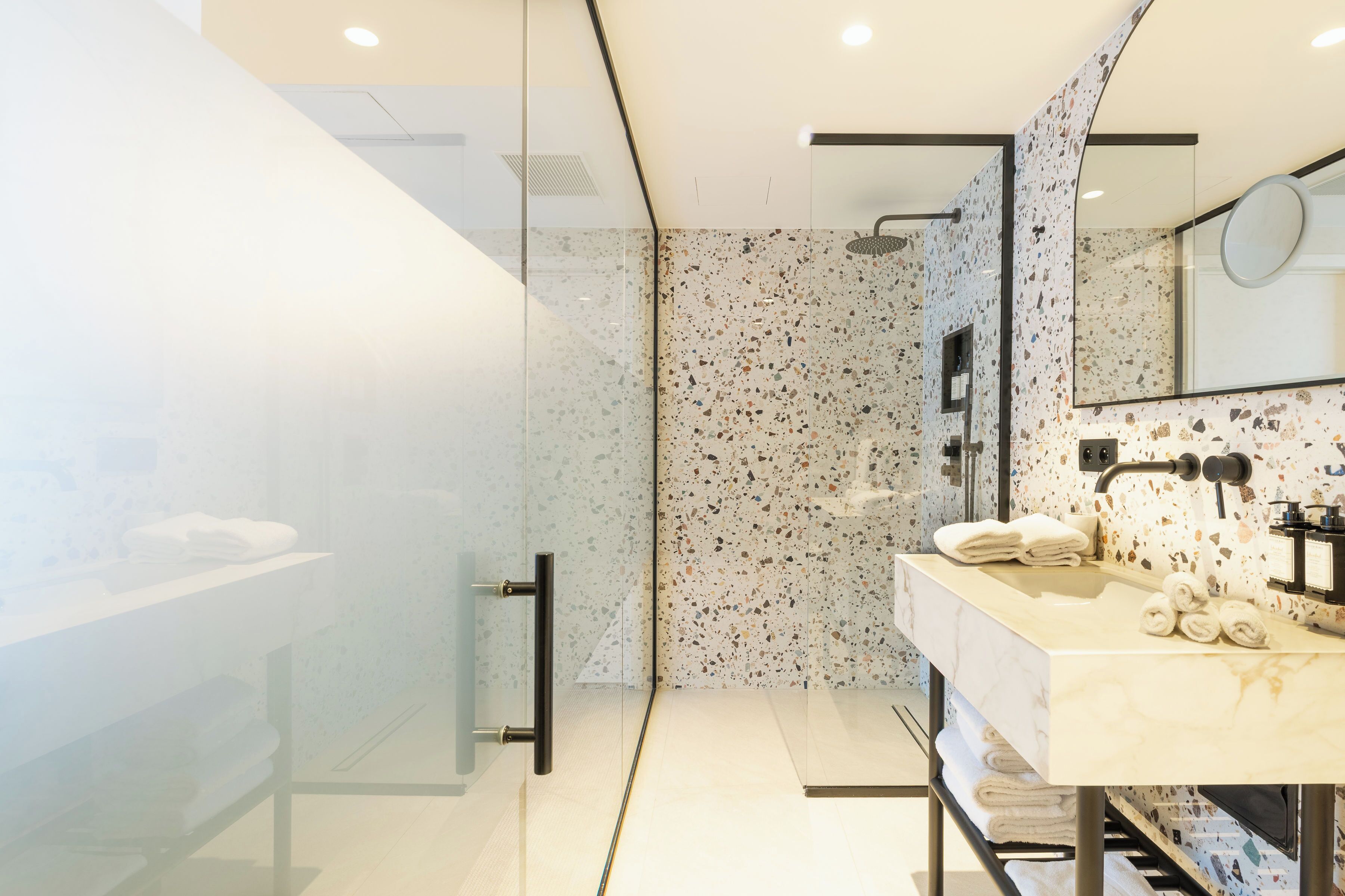 Un baño moderno con cabina de ducha de vidrio, lavamanos de mármol y un espejo grande.
