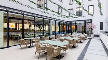 An outdoor café area with tables and chairs, a glass wall, and a decorative plant.