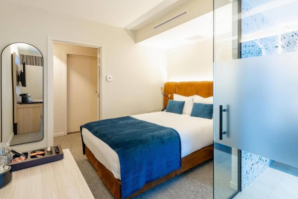 A hotel room with a bed, a bedside table with a tray, a mirror, and a wardrobe.