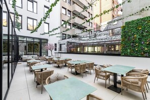 An indoor patio area with tables and chairs, a glass wall, and a green wall with plants. - The Liman Hotel (Brussels)