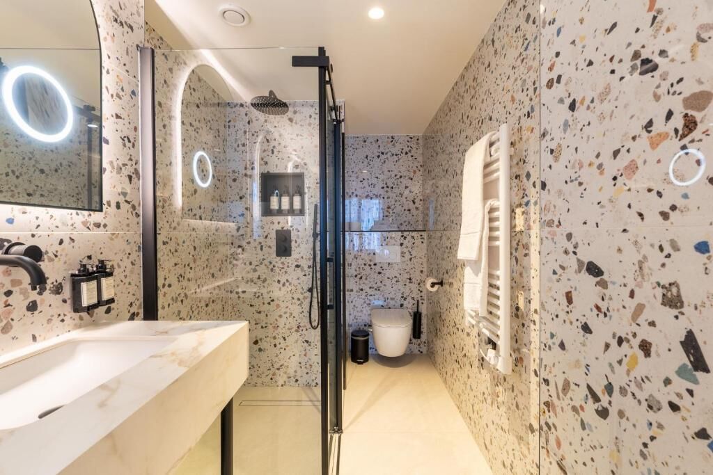 A modern bathroom with a glass-enclosed shower, a large mirror with a ring light, and a freestanding toilet.