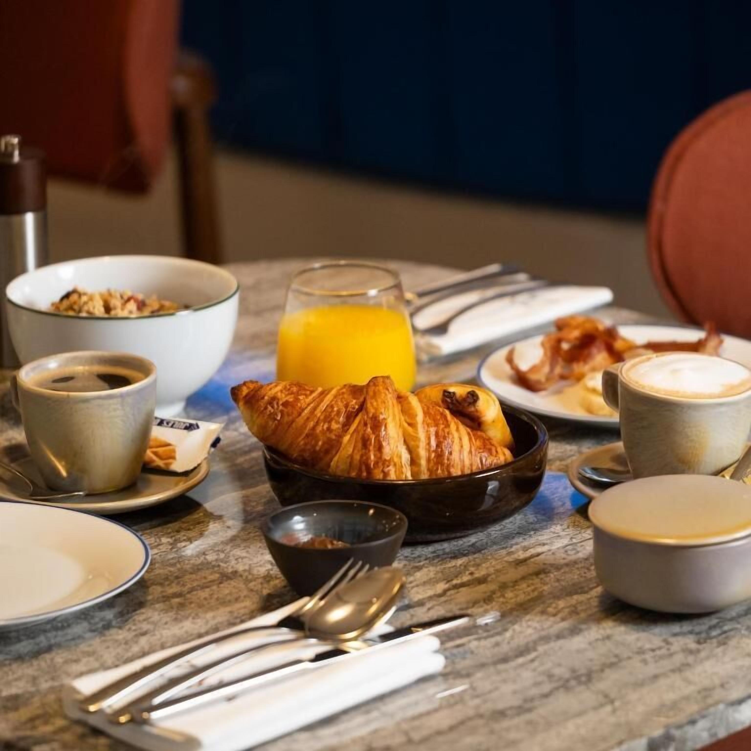A breakfast table with croissants, coffee, orange juice, and a bowl of cereal.