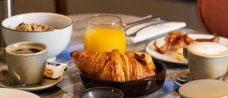 Una mesa de desayuno con cruasanes, café, jugo de naranja y un tazón de cereal.