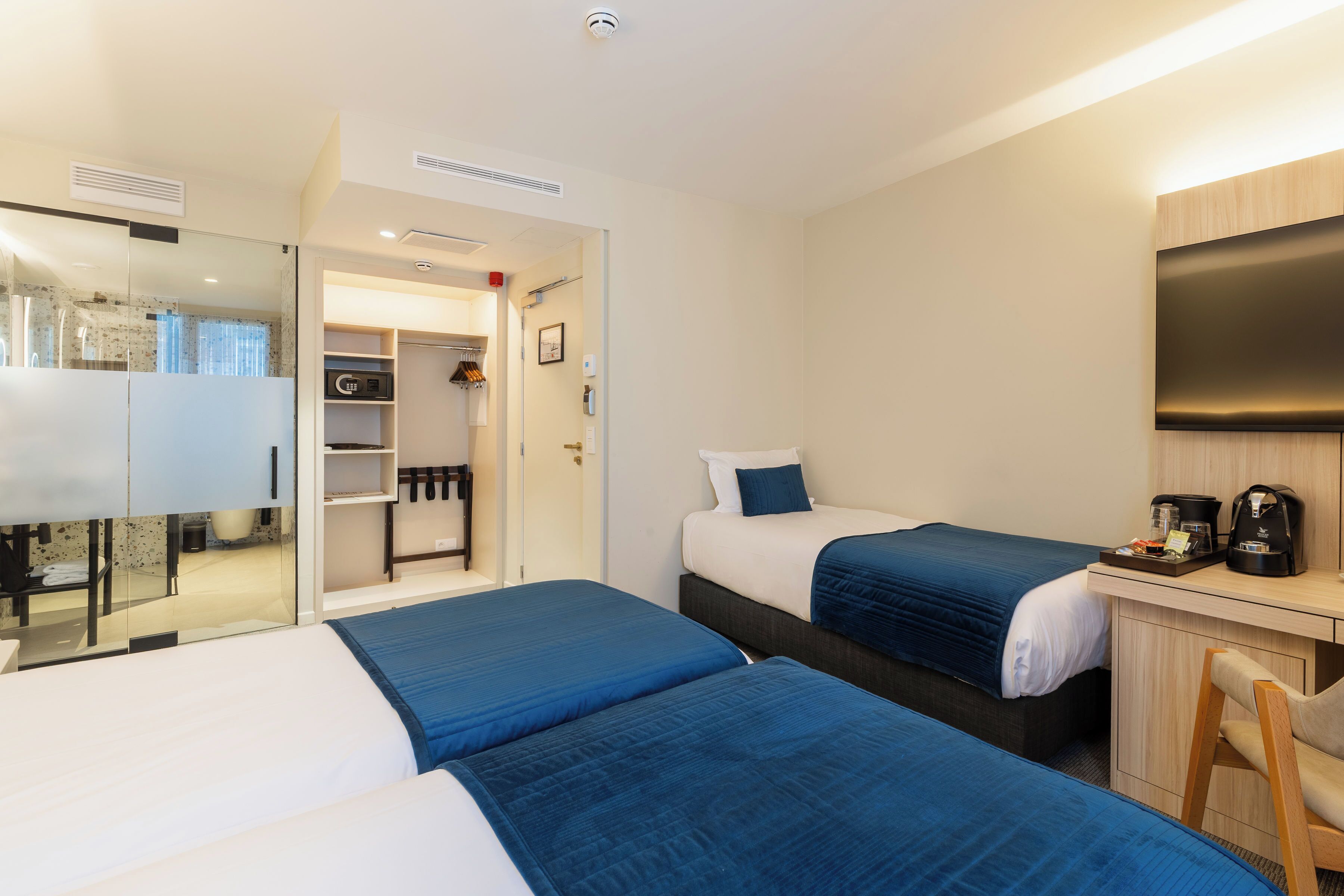Habitación de hotel con dos camas, un escritorio, una silla, un televisor y un vestidor.
