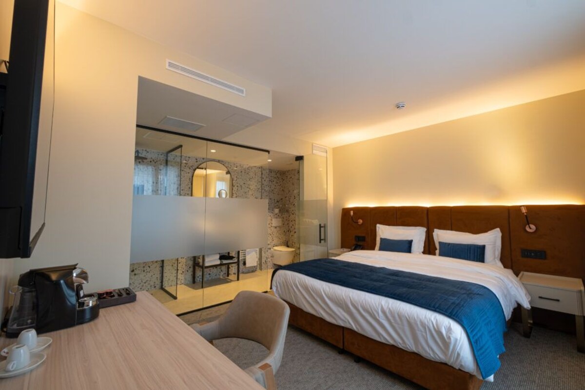 A hotel room with a bed, bedside table, chair, and a coffee maker.
