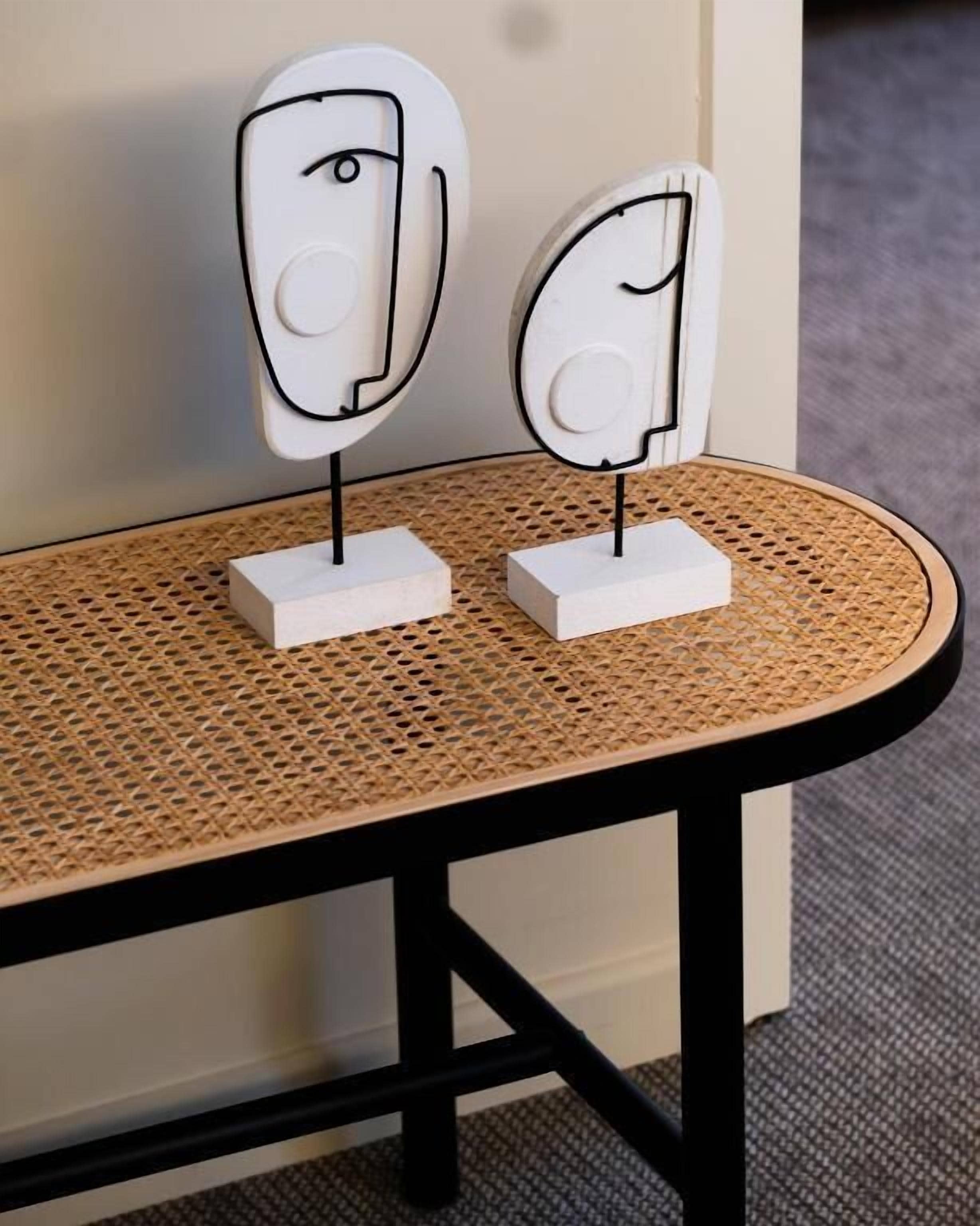 Twee witte, abstracte kunstwerken op een rond, geweven bijzettafeltje met een zwarte lijst.