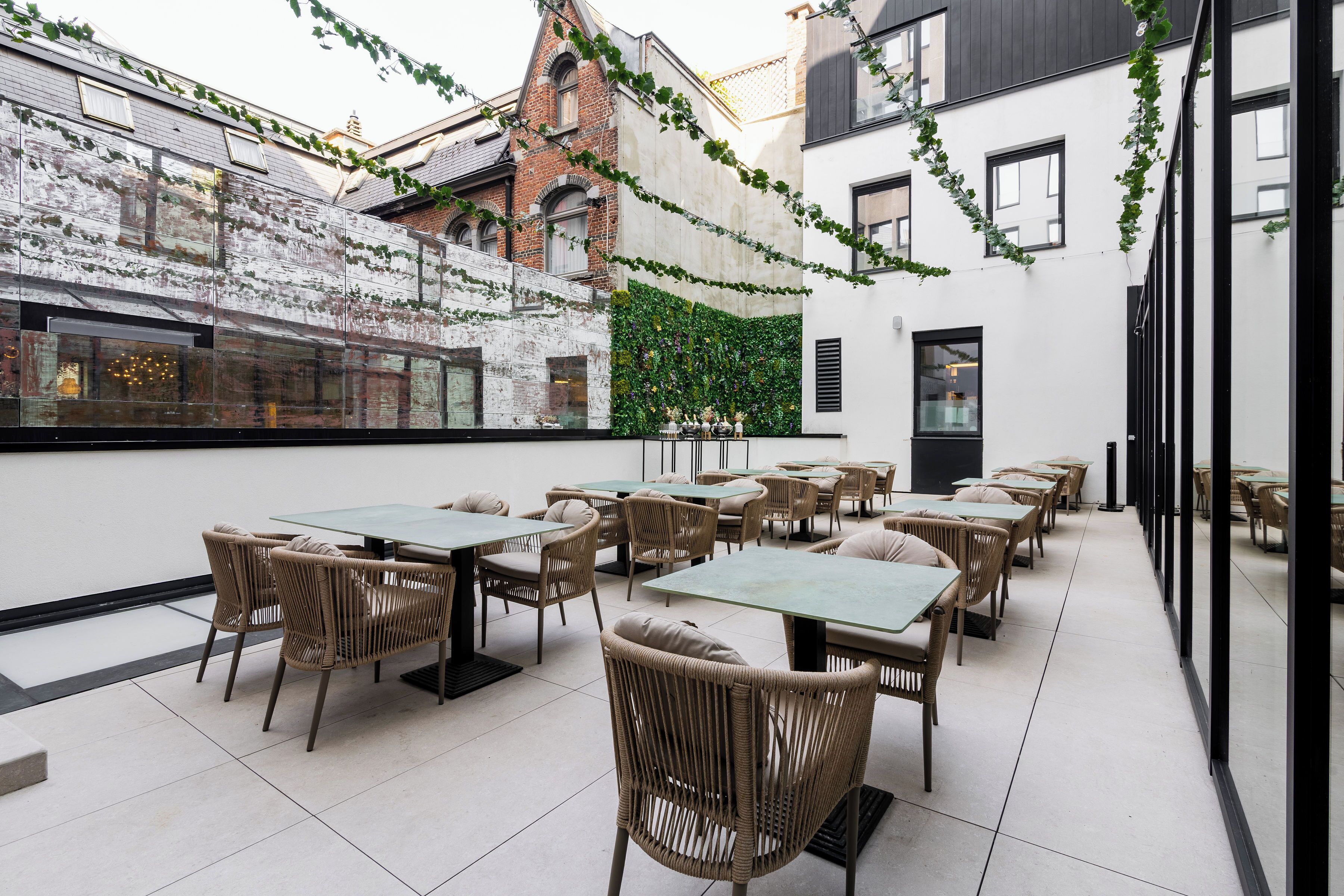 A restaurant with outdoor seating, a brick wall, and a green vine-covered wall.