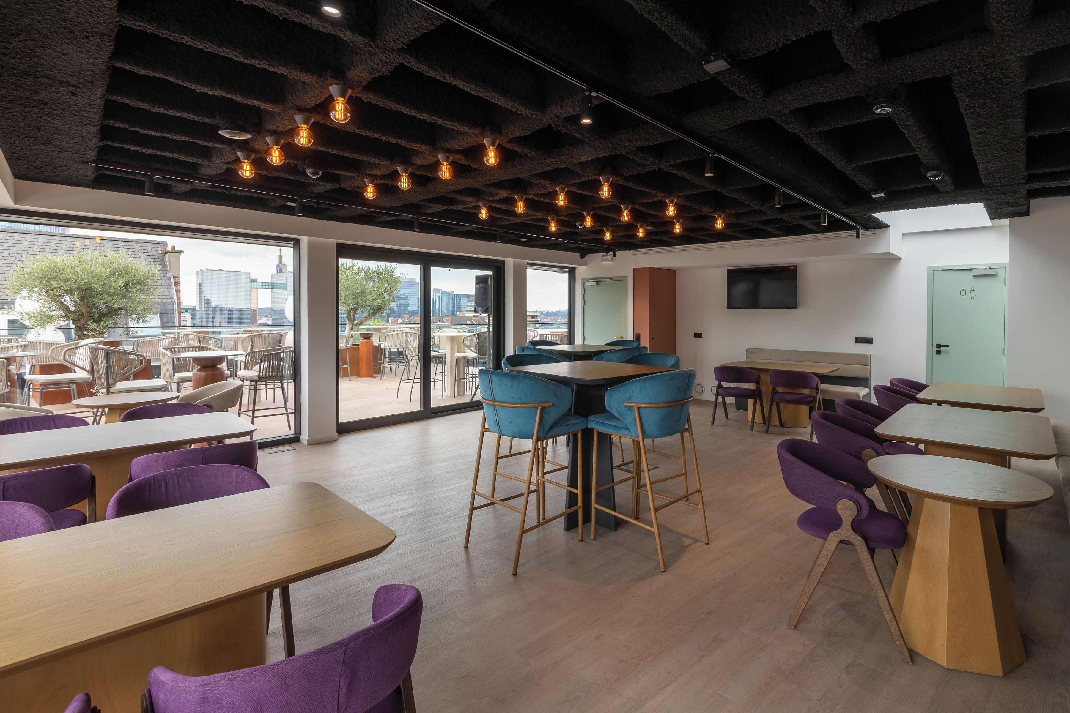 A modern interior with tables and chairs, large windows, and a city view.