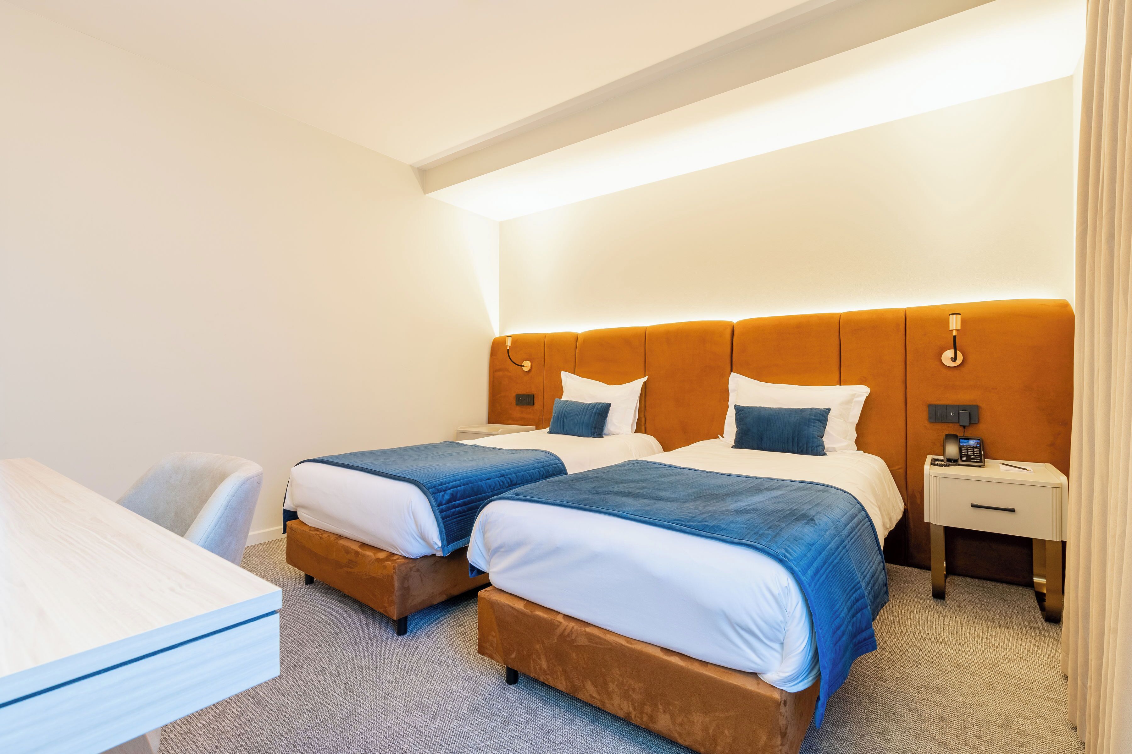 A hotel room with two beds, a desk, and a nightstand with a phone.