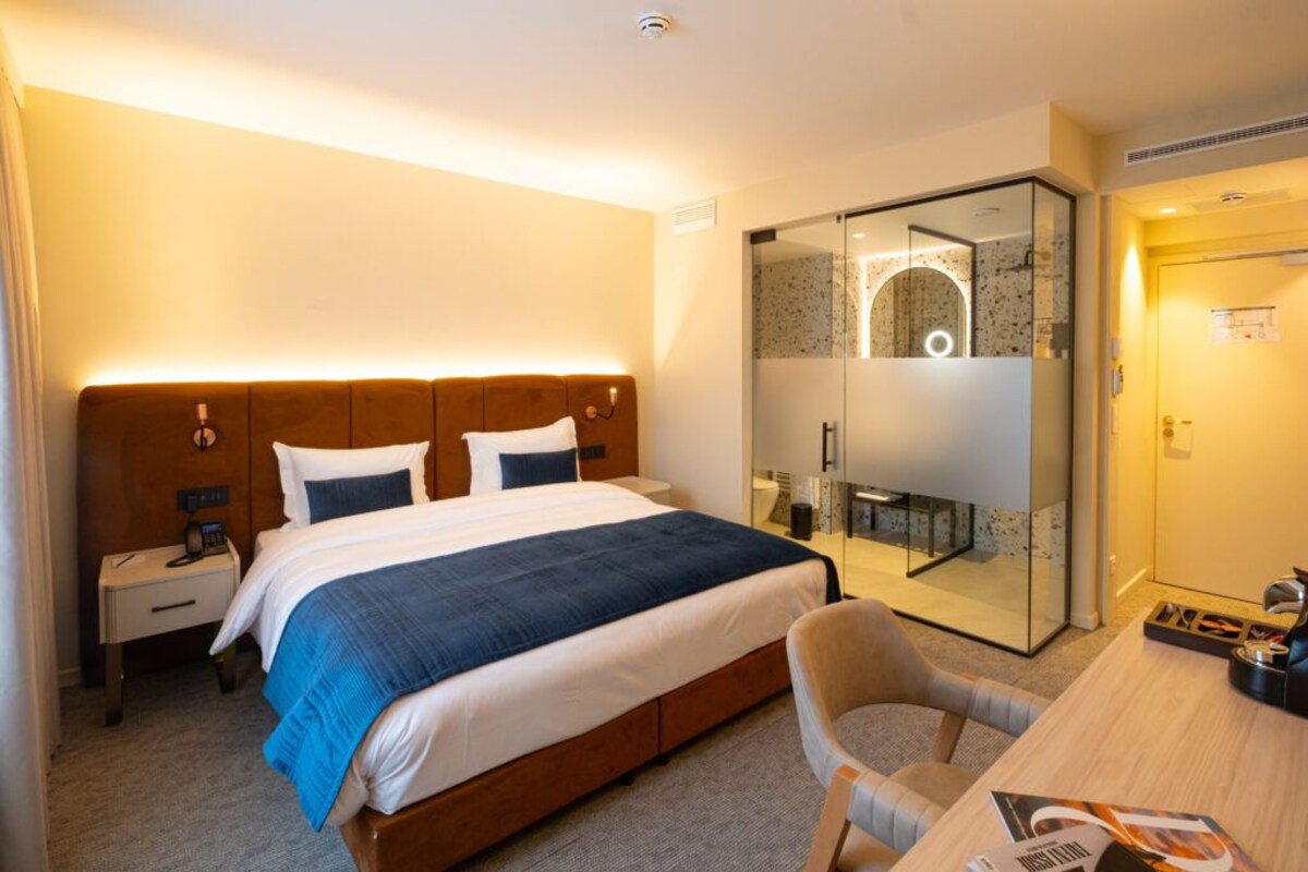 A hotel room with a bed, bedside table, chair, desk, and a glass-enclosed shower area.