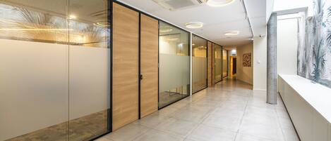 A modern hallway with glass partitions, recessed lighting, and a tiled floor.