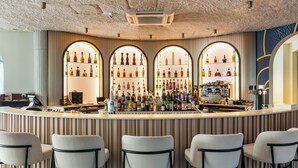 A bar area with three arched shelves displaying bottles, a coffee machine, and bar stools. - The Liman Hotel (Brussels)