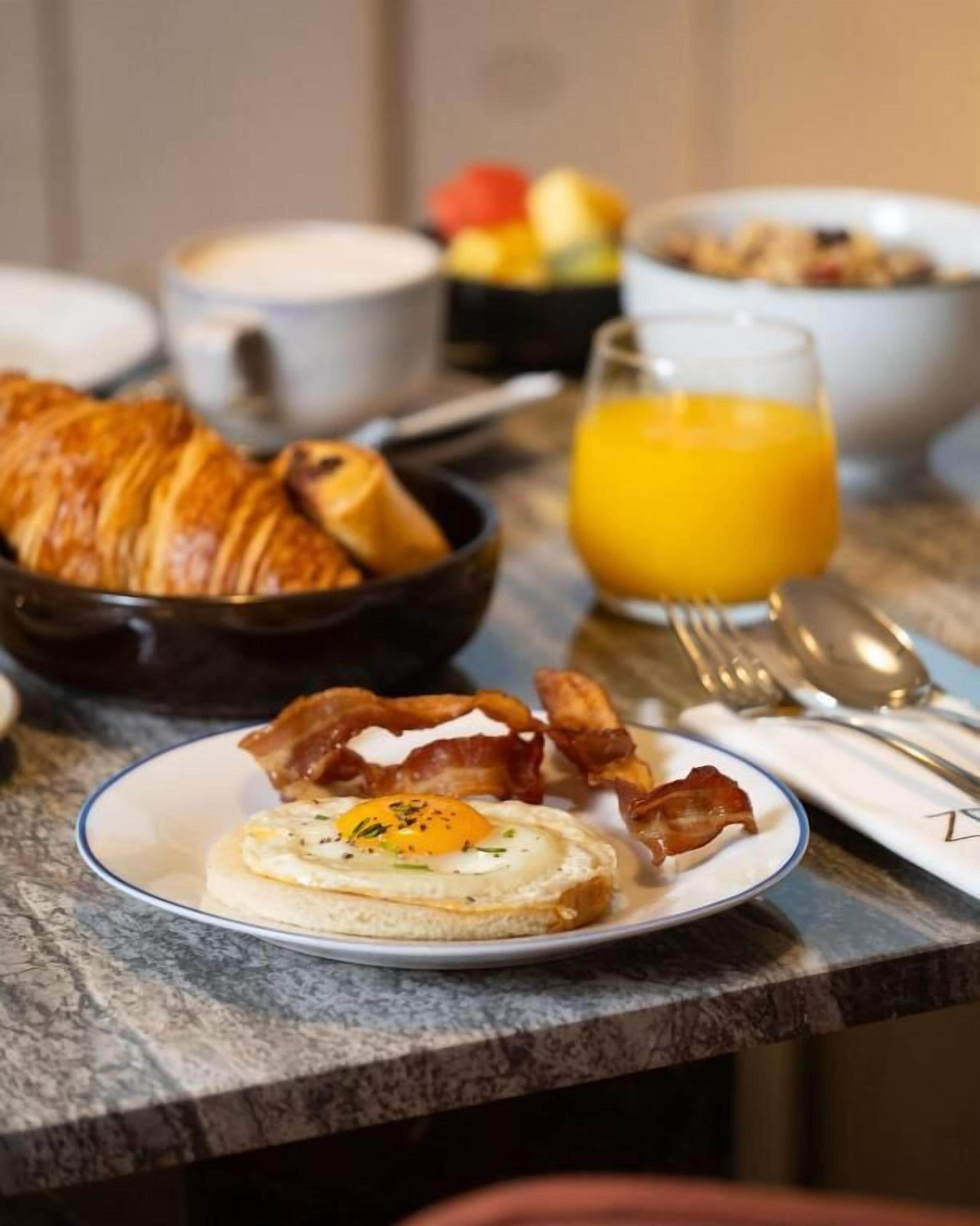 A breakfast table with eggs, bacon, toast, and orange juice.