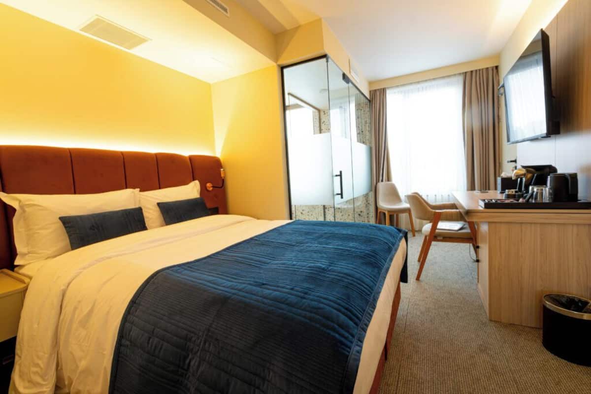 A hotel room with a bed, a desk, a chair, and a television.