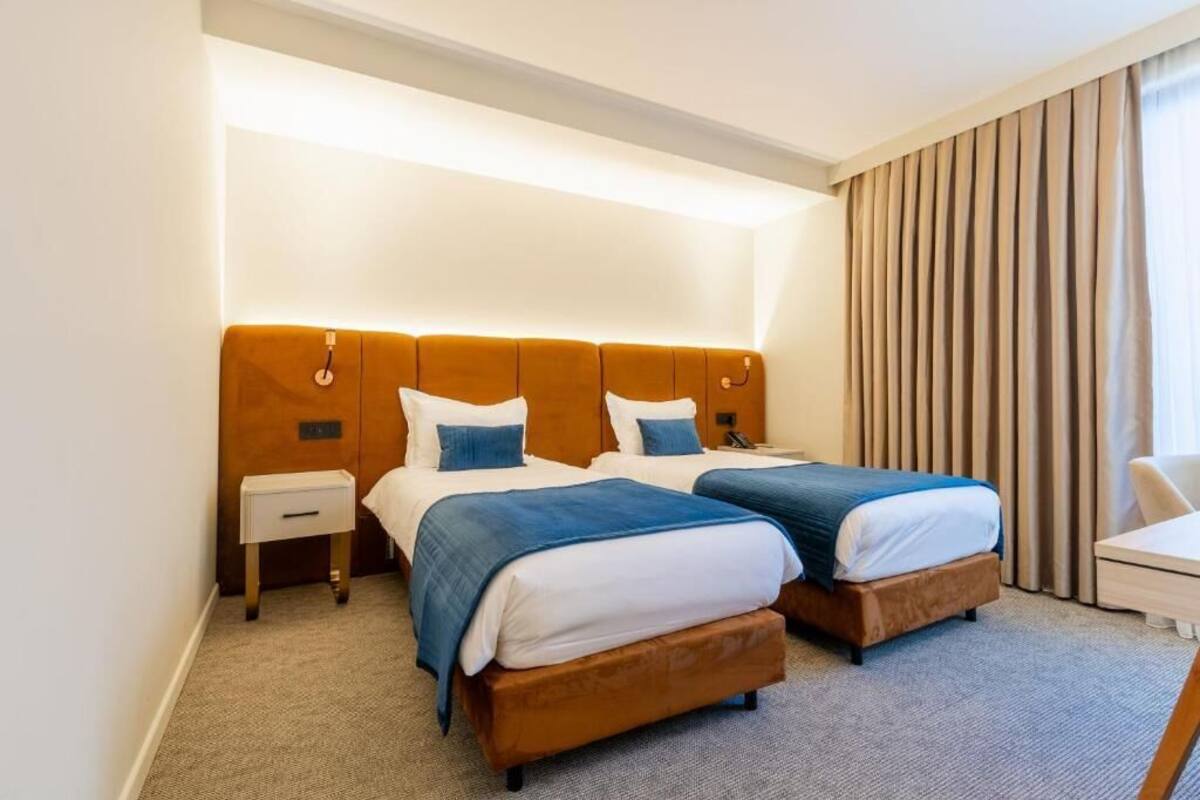 A hotel room with two beds, a nightstand, a desk, and a large window with curtains.