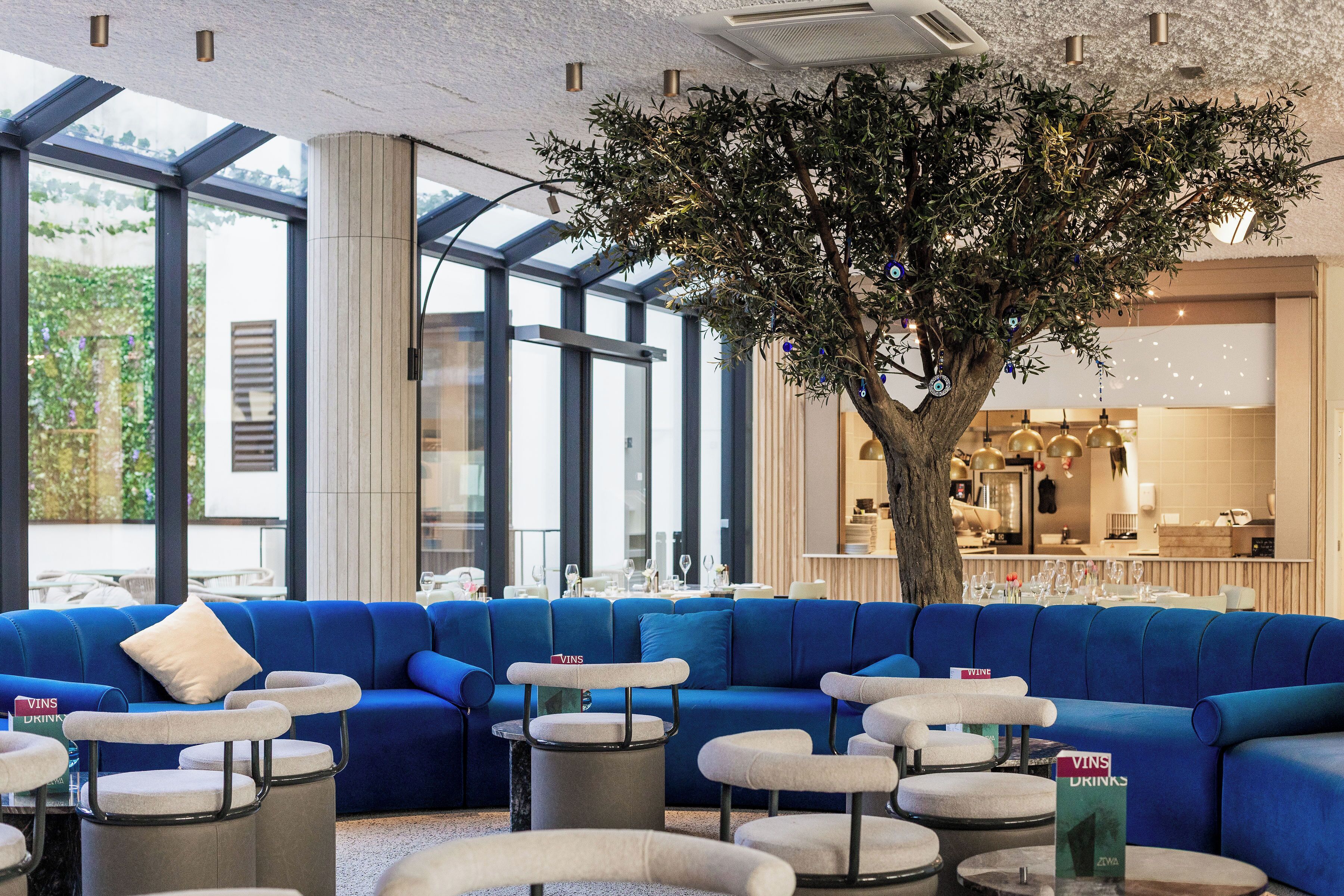 Un interior moderno con un sofá azul, mesas redondas y un árbol central.