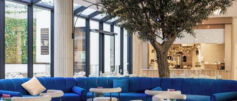 Un interior moderno con un sofá azul, mesas redondas y un árbol central.