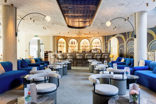 A modern lounge area with sofas, armchairs, and a bar with shelves of bottles. - The Liman Hotel (Brussels)