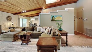 Ein geräumiges Wohnzimmer mit hoher Decke, Holzbalken, einer großen Sofagarnitur, einem Couchtisch und einem Essbereich im Hintergrund.