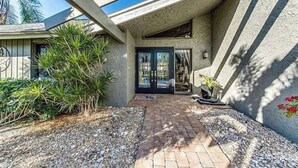 Ein modernes Haus mit geneigtem Dach, einer Terrasse mit Pflasterboden und einer großen Glasdoor, die zum Innenbereich führt.