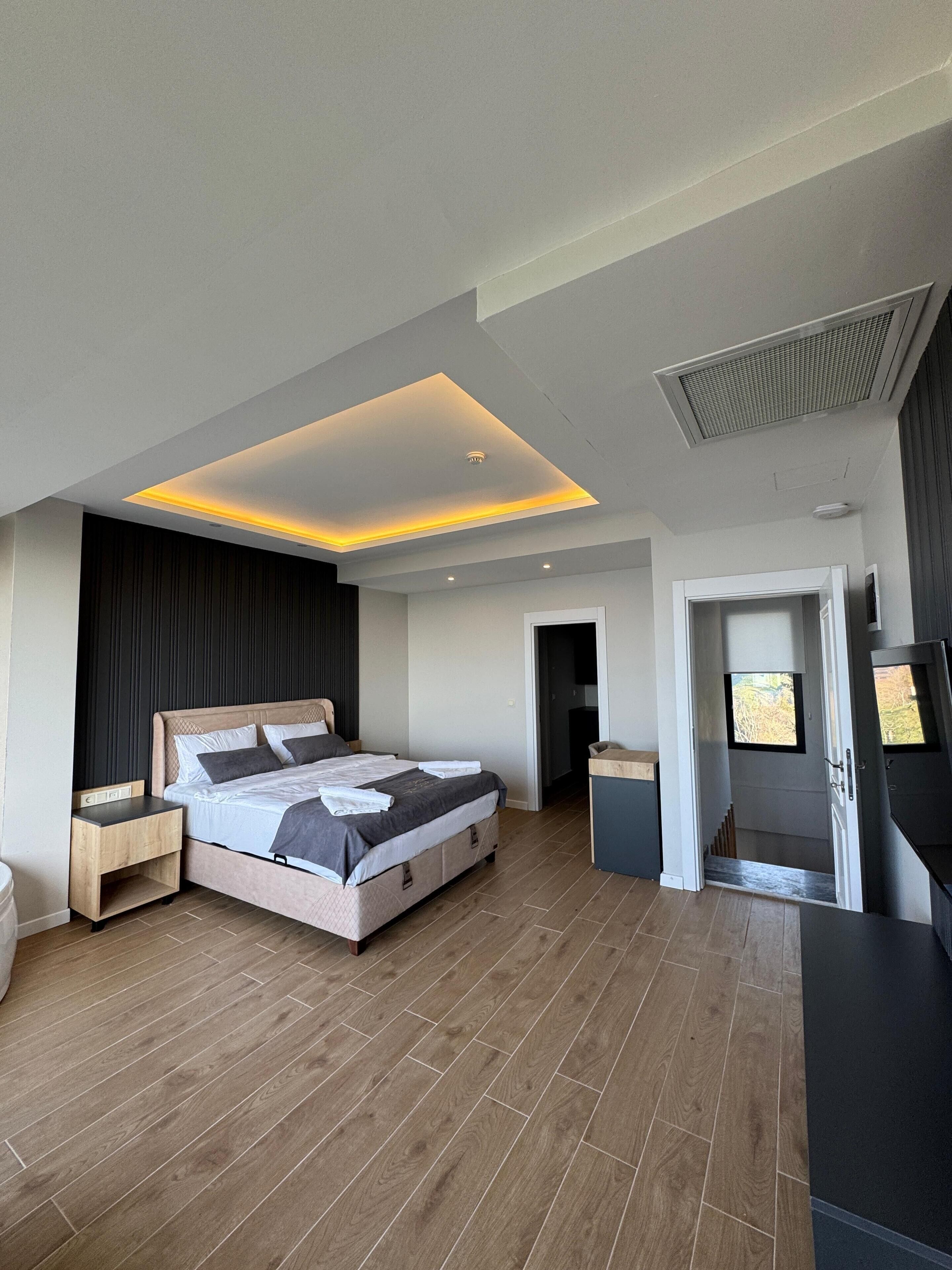 A modern bedroom with a large bed, wooden flooring, and a ceiling with recessed lighting.