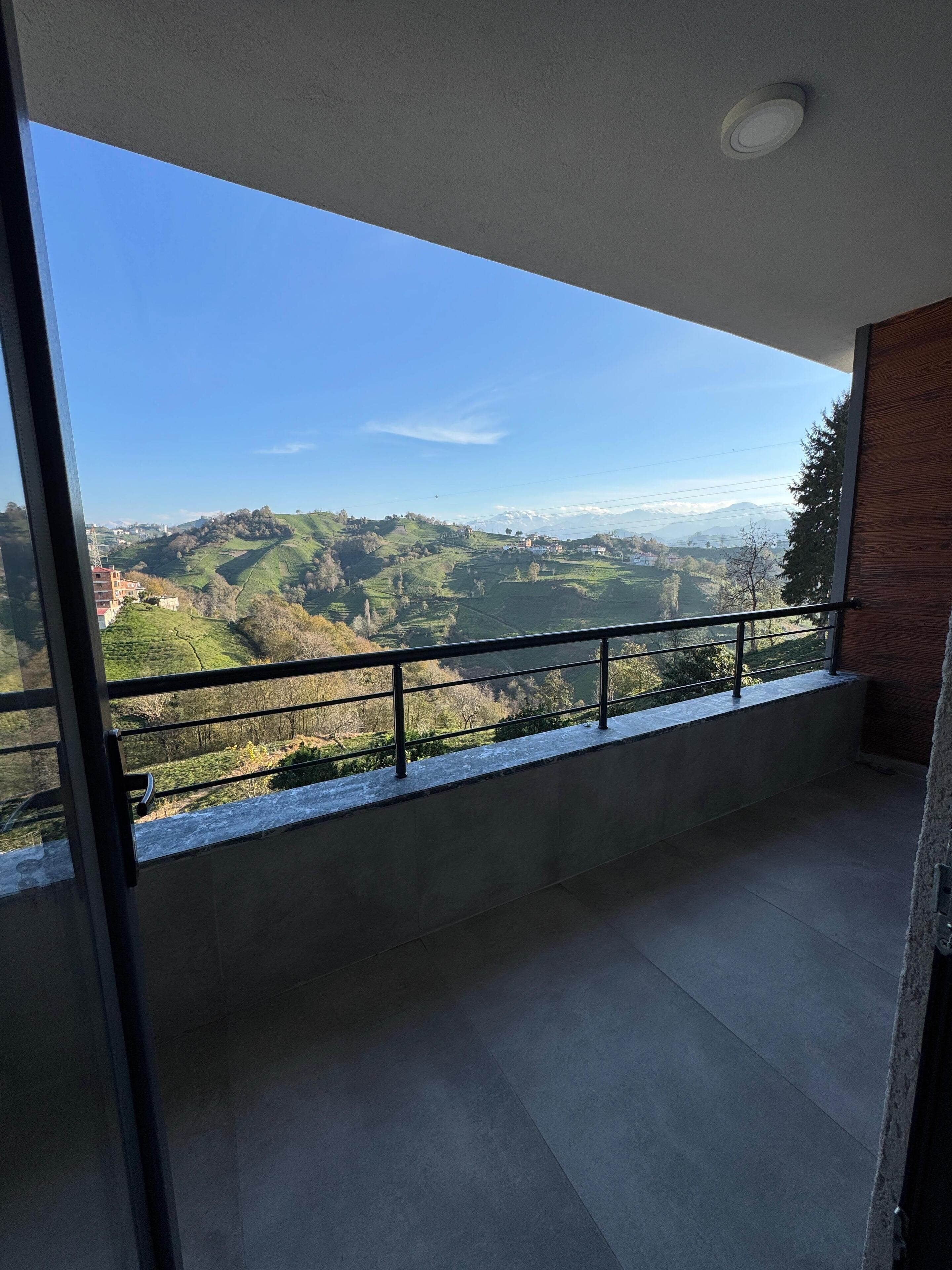 A balcony with a view of a hilly landscape and distant mountains.