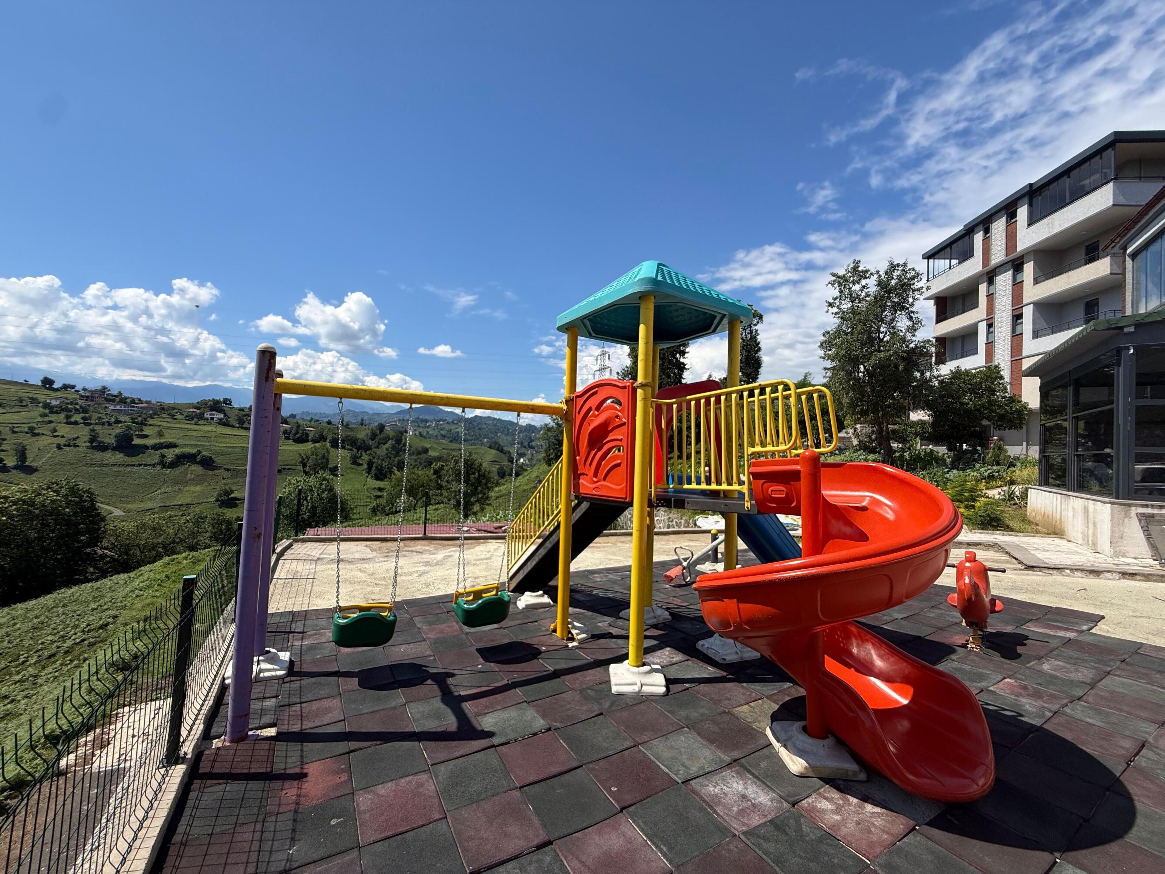 Une aire de jeux avec des balançoires, un toboggan et une structure d’escalade.