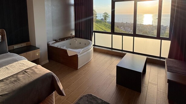A modern bedroom with a large window, a bed, a sitting area, and a bathtub. - NORTH STAR RESORT HOTEL (Of)