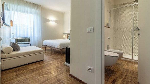 A modern hotel room with a bed, a sofa, a small table, and a shower area. - Il Faro luxury rooms & lounge (La Spezia)