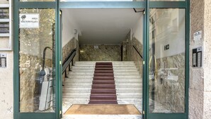 Una escalera conduce a la entrada de un edificio con paredes de mármol y una puerta de cristal.