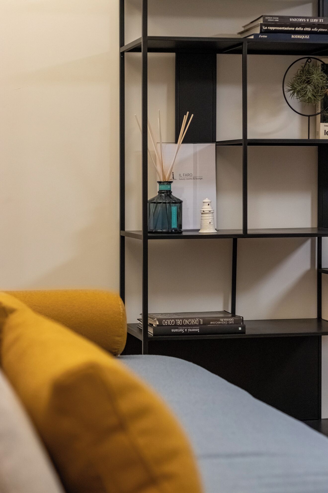 A modern living room with a black bookshelf, a blue vase with reed sticks, and a white candle.