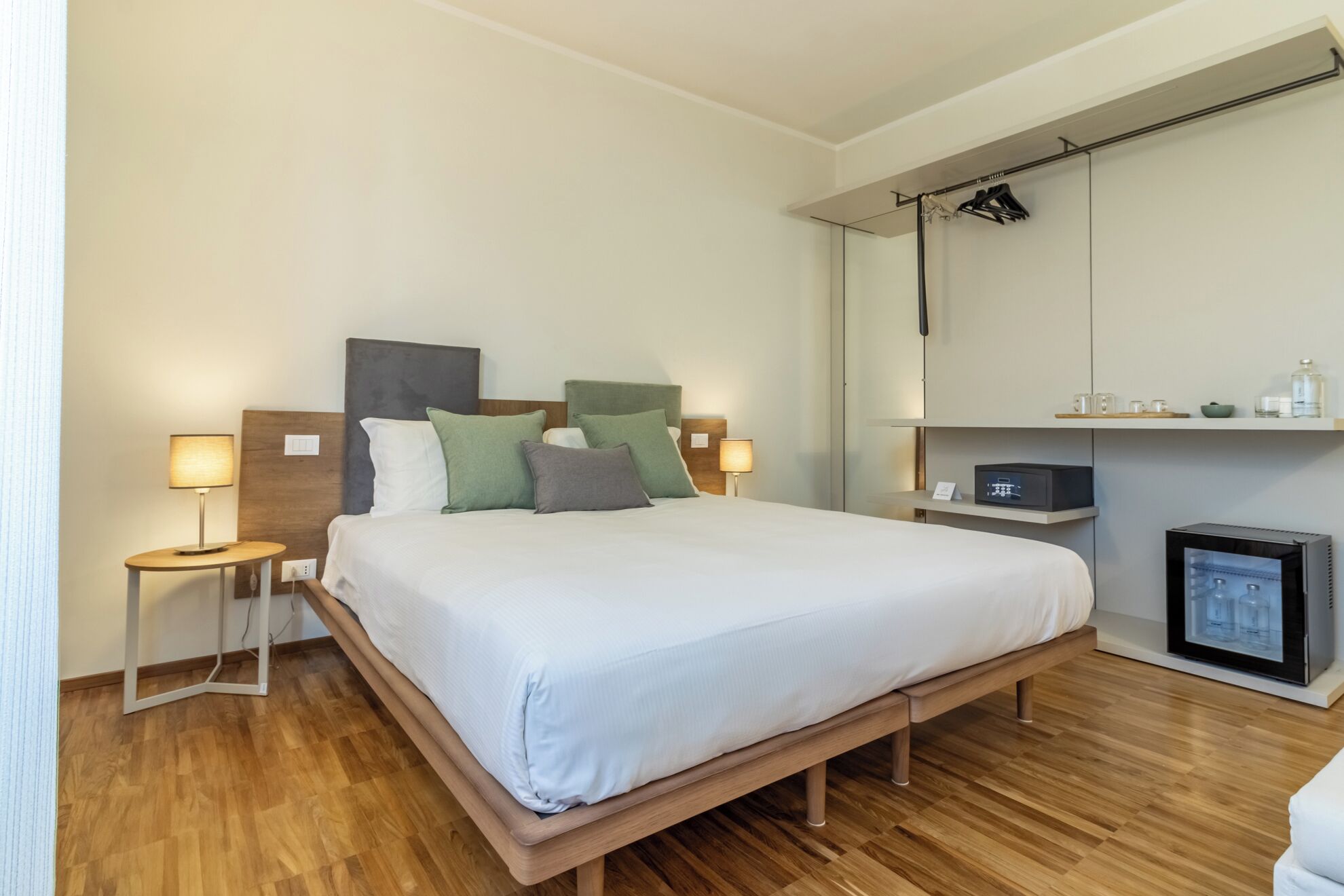 Ein modernes Hotelzimmer mit einem hölzernen Bett, zwei Nachttischen mit Lampen, einem Flachbildfernseher und einer Minibar.