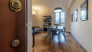 Un interior moderno con piso de madera, una zona de comedor con mesa y sillas, un sofá, una estantería y un ventanal con vistas al exterior.