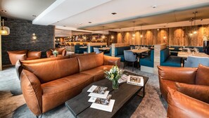 A modern lounge area with leather sofas, a coffee table with magazines, and a bar in the background.