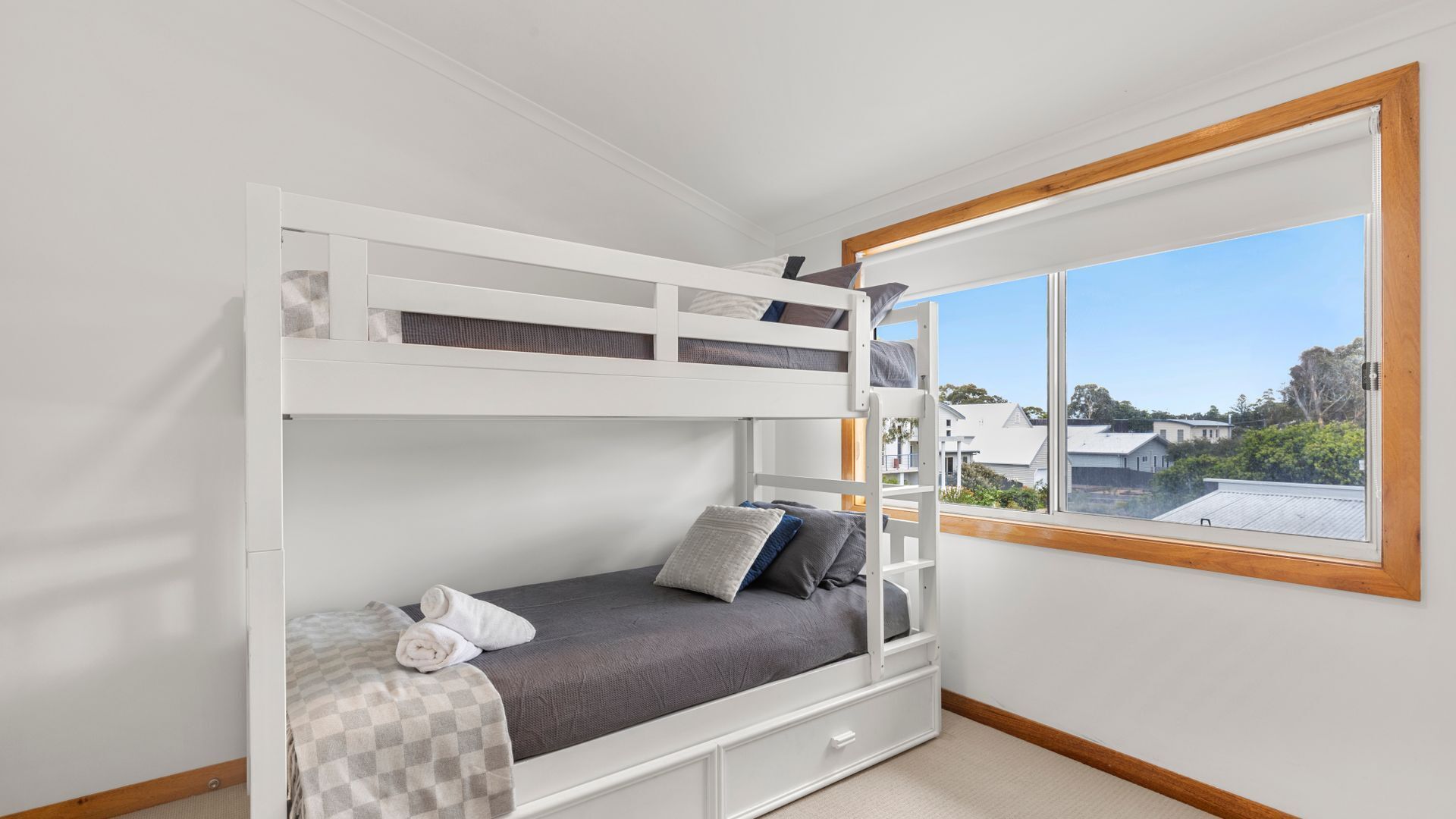 A bunk bed room with a window, a view of houses, and a checkered blanket on the lower bunk.