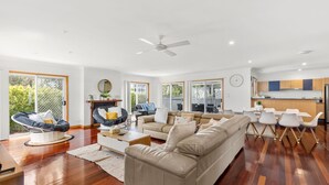 A spacious living room with a beige sofa, a round coffee table, and a dining area with white chairs.