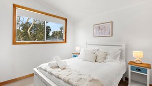 A bedroom with a large window, a bed with white bedding, two bedside tables, and a framed picture on the wall.