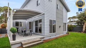 A two-story house with a covered patio, a dining area with outdoor furniture, and a well-maintained lawn.