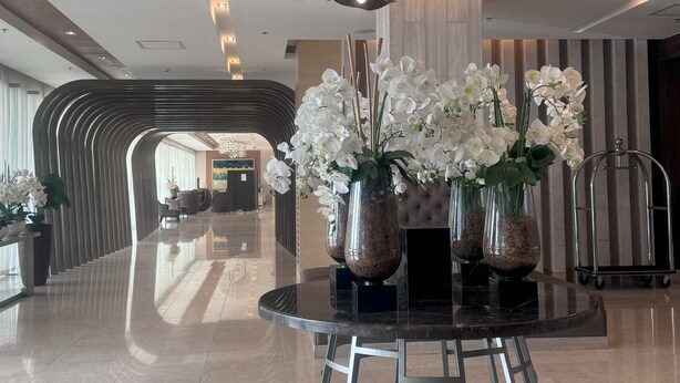 Een moderne lobby met een ronde glazen tafel, witte orchideeën en een bijzondere plafondlamp.