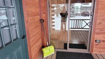 L’entrée d’un chalet en bois, avec une porte verte, une porte-fenêtre coulissante et un balai appuyé contre le mur.